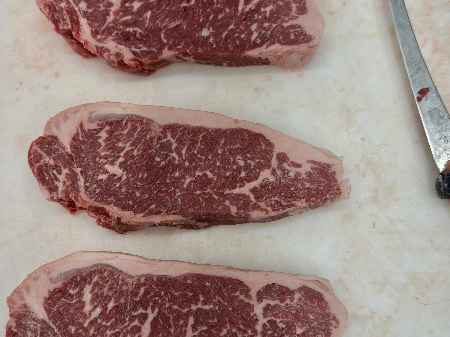 Three marbled New York strip steaks on the cutting board next to a boning knife